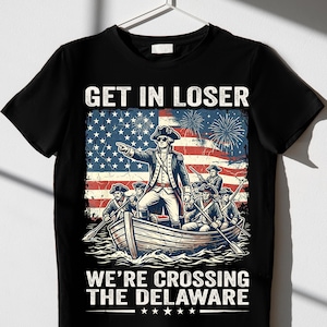 May include: Black t-shirt with a graphic design featuring a historical illustration of a boat crossing the Delaware River, with the text "GET IN LOSER WE'RE CROSSING THE DELAWARE". The design includes the American flag and fireworks.