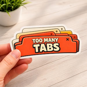May include: A sticker with the text "TOO MANY TABS" in white letters on an orange background. The sticker has a layered design with beige, yellow, and orange tabs. The sticker is held by a hand.