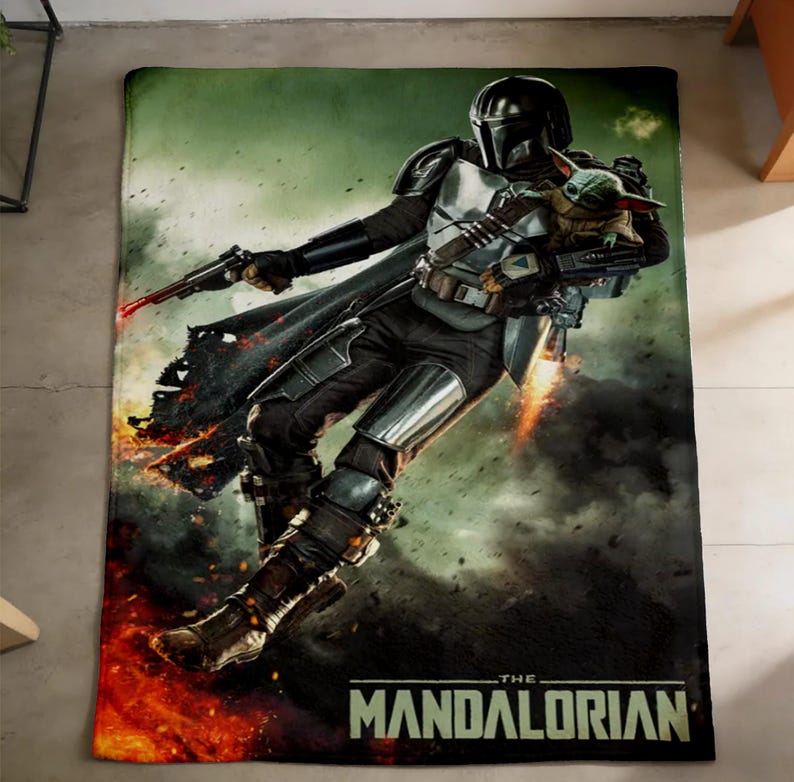 May include: A rectangular blanket featuring The Mandalorian, holding a blaster and Grogu. The design includes a dark colour palette with fiery orange and green hues, and the text "THE MANDALORIAN" at the bottom.