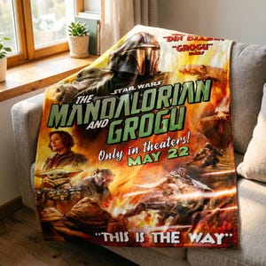 May include: A Star Wars themed blanket featuring the Mandalorian and Grogu. The blanket has a vibrant design with the text "The Mandalorian and Grogu" and "This is the Way". The blanket is draped over a grey sofa.