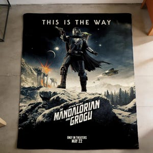 May include: Black blanket with a scene from The Mandalorian. The image shows the Mandalorian with Grogu. Text reads "THIS IS THE WAY" and "THE MANDALORIAN AND GROGU". The blanket is a Star Wars themed product.
