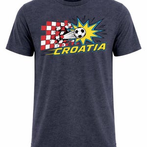 Op de afbeelding: Marineblauw t-shirt met een afbeelding van een voetbal die door een rood-wit geblokt patroon breekt. Het woord "CROATIA" is geel geschreven met een blauwe omlijning.
