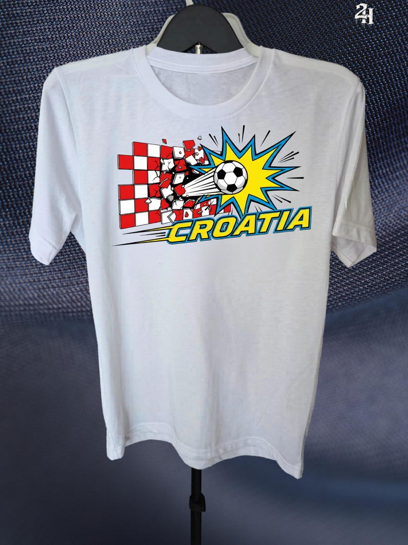 Puede incluir: Una camiseta blanca de manga corta con un gr&aacute;fico de un bal&oacute;n de f&uacute;tbol atravesando una pared de cuadros rojos y blancos. El dise&ntilde;o incluye un fondo de estrella amarilla y la palabra CROATIA en letras amarillas con un borde azul.