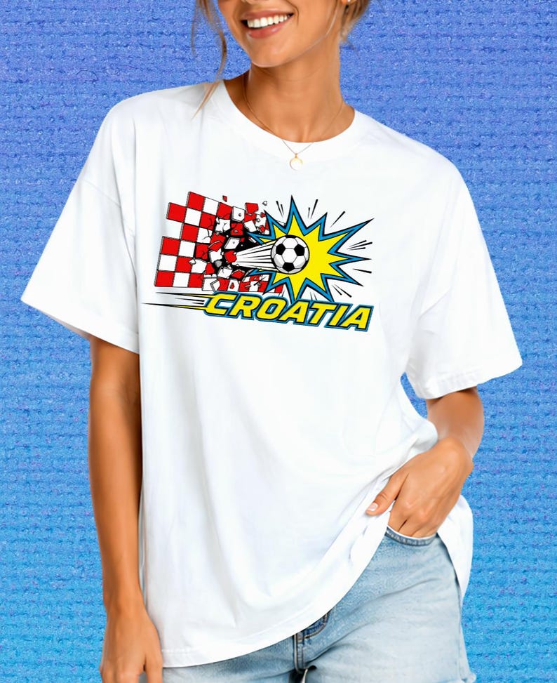 Puede incluir: Una camiseta blanca de manga corta con un estampado gr&aacute;fico de un bal&oacute;n de f&uacute;tbol atravesando una pared de cuadros rojos y blancos. El dise&ntilde;o incluye un efecto de estrella amarilla y la palabra CROATIA en letras azules con bordes amarillos.