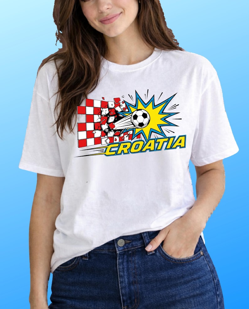 Puede incluir: Una camiseta blanca de manga corta con un gr&aacute;fico de un bal&oacute;n de f&uacute;tbol atravesando una pared de cuadros rojos y blancos. El dise&ntilde;o incluye un efecto de estallido amarillo y la palabra CROATIA en letras amarillas con borde azul.