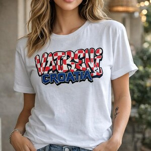 May include: White t-shirt with the text "VATRENI CROATIA" in a red, white, and blue design. The text is in a graffiti-style font. The shirt has short sleeves and a crew neck.