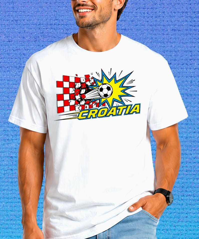 Puede incluir: Una camiseta blanca de manga corta con un estampado gr&aacute;fico de un bal&oacute;n de f&uacute;tbol atravesando una pared de cuadros rojos y blancos. El dise&ntilde;o incluye un efecto de estallido amarillo y la palabra CROATIA en letras amarillas con borde azul.