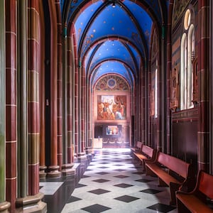 Pode incluir: Vista interior de um corredor de catedral com um teto azul adornado com estrelas douradas e desenhos florais. O corredor apresenta tetos arqueados, colunas altas e um chão xadrez em preto e branco. Bancos de madeira alinham as paredes.