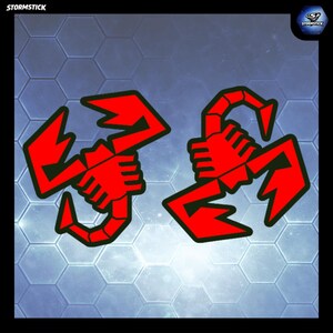 May include: Two red scorpion decals with black outlines, featuring stylised segmented bodies and large pincers. The word STORMSTICK appears in the top left corner and a circular logo with the text STORMSTICK is in the top right corner.