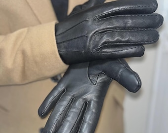 May include: A pair of black leather gloves featuring visible stitching along the fingers and back of the hand. The gloves have a smooth texture and a tailored fit, with reinforced seams at the fingertips and a clean, minimalist design.
