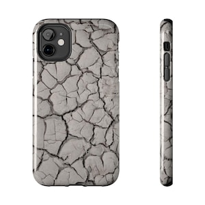 Puede incluir: Funda de teléfono con un diseño de tierra agrietada en tonos grises y blancos. La funda tiene un acabado brillante y un recorte negro para la lente de la cámara. Vista lateral del perfil delgado y los botones.