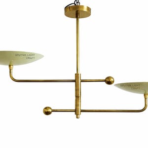May include: A brass Sputnik-style chandelier with two curved arms, each holding a saucer-shaped light fixture. The fixture has a central vertical rod and a circular ceiling mount. The text "SPUTNIK LIGHT CRAFT" is visible on the light fixtures.