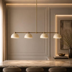 May include: A linear pendant light fixture featuring a long, thin brass-toned metal rod suspended from the ceiling. Four matte cream-colored dome-shaped shades are attached to the horizontal bar, each emitting a soft, warm downward glow.