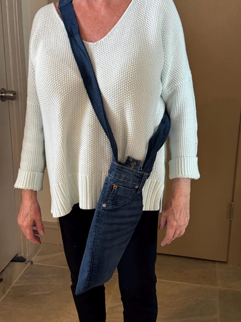 May include: A denim crossbody bag made from repurposed jeans. The bag features the front pockets and waistband of the jeans, with a long strap for over-the-shoulder wear. The denim is a medium wash blue.