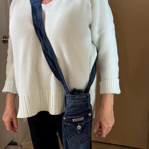 May include: A denim crossbody bag made from repurposed jeans. The bag features the back pocket of the jeans, complete with the original hardware and a button closure. The strap is made from the same denim material.