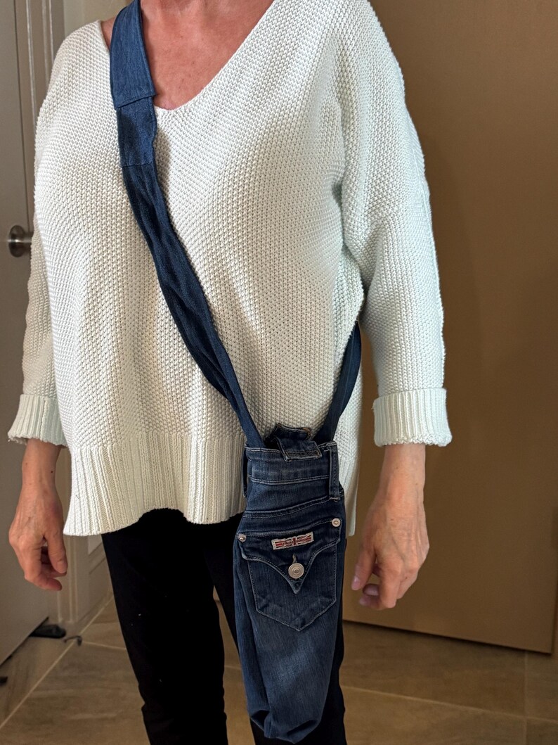 May include: A denim crossbody bag made from repurposed jeans. The bag features the back pocket of the jeans, complete with the original hardware and a button closure. The strap is made from the same denim material.