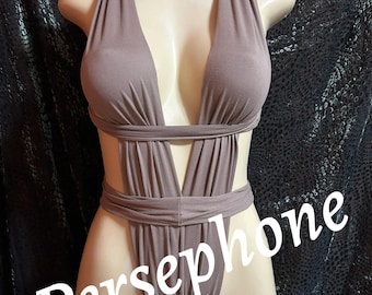 May include: A taupe-colored one-piece swimsuit featuring a deep plunging neckline, wide shoulder straps, and horizontal bands across the midsection that create cut-out sides. The word Persephone is printed in white text across the front.