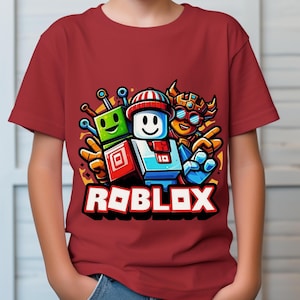 May include: A maroon t-shirt featuring a colorful graphic of three cartoon characters and the word "ROBLOX" in white block letters. The characters are in various colors, including green, blue, and orange.
