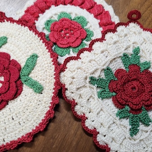 May include: Three handmade crochet pot holders in a cream color with red and green floral designs. One is round, one is square, and one is a half-circle shape. The edges are trimmed in red.