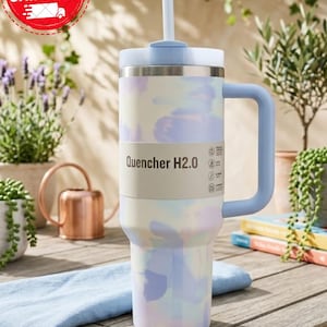 Puede incluir: Un vaso grande y aislado con asa y pajita. El vaso presenta un estampado tie-dye pastel en tonos azules, morados y amarillos. El texto "Quencher H2.0" est&aacute; impreso en el lateral. La tapa y el asa son de color azul claro.