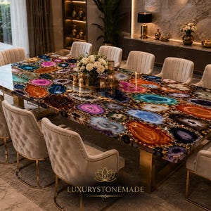 May include: A rectangular dining table featuring a polished surface composed of multicolored agate slices in shades of blue, purple, orange, and pink, supported by gold-toned metal legs, surrounded by ten beige upholstered chairs with gold trim.