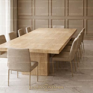 Puede incluir: Una gran mesa de comedor rectangular de piedra de color claro con una base de pedestal a juego. Ocho sillas tapizadas beige con patas doradas rodean la mesa. La habitación tiene paredes de color claro y un suelo de mármol. El texto "LUXURYSTONEMADE" está en la parte inferior.