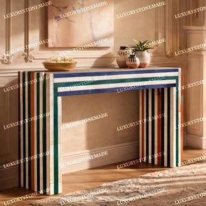 May include: A decorative console table with a striped design in shades of blue, green, orange, and black. The table is in a room with a fireplace and a rug. The table's dimensions are approximately 48 inches wide, 16 inches deep, and 30 inches high.