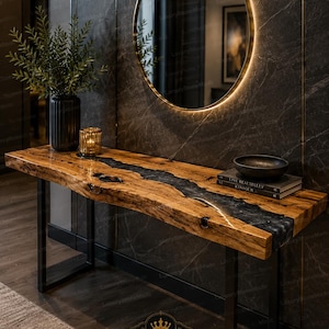 May include: A rectangular console table featuring a natural live-edge wood slab with a central black resin river inlay, supported by black metal legs. The table holds a black vase with greenery, a gold candle holder, and two stacked books.