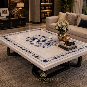Pode incluir: Uma mesa de centro retangular de mármore branco com um intrincado padrão floral azul incrustado ao longo da borda e um medalhão central. A mesa é sustentada por uma base de metal preto e exibe o texto LUXURYSTONEMADE na parte inferior.