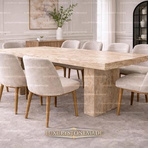 May include: A white ceramic mug with a black handle and the text "But First, Coffee" in a bold, black font. The mug is set against a blurred background, suggesting a cozy setting.