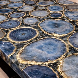 Luxury blue agate crystal dining table top made from natural gemstone slices arranged into polished slab surface showcasing vibrant banded mineral patterns ideal for modern dining interiors and high end residential homes across the United States. Elegant agate gemstone furniture creates bold statement centerpiece for designer spaces.