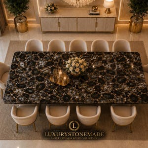 May include: An overhead view of a dining room with a large, rectangular table. The table has a black and gold patterned surface and is surrounded by ten beige chairs. A floral arrangement and candles sit on the table. The room has a neutral color palette.