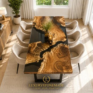May include: A large, rectangular dining table with a unique wood grain pattern and a black epoxy river. The table is surrounded by eight beige upholstered chairs. The table has a black metal base. The room has hardwood floors and large windows.