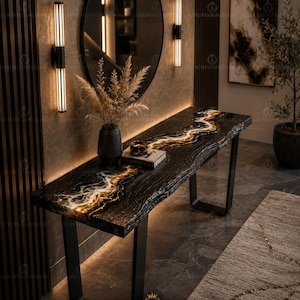Pode incluir: Uma consola de resina epóxi preta e dourada com um design de borda viva. A mesa tem uma estrutura de metal preta e é iluminada com iluminação quente. A mesa está em um ambiente interior moderno com um espelho e arandelas.