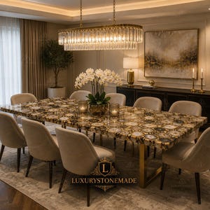 May include: A luxurious dining room set featuring a large rectangular table with a unique agate stone top. The table is surrounded by beige upholstered chairs. A gold chandelier hangs above, illuminating the room. The room includes a large painting and a black cabinet.