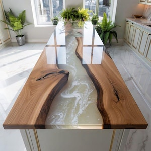 May include: A bespoke kitchen island with a river table design. The table has a light-coloured epoxy resin river between two pieces of natural wood. The wood has a warm, brown tone, and the island is set in a bright kitchen with a tiled floor.
