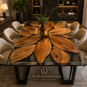 May include: A modern dining table with a unique design. The table features a clear glass top with a wooden leaf-like pattern. It is supported by a black metal base and surrounded by beige upholstered chairs. The table is from Luxury Stone Made.