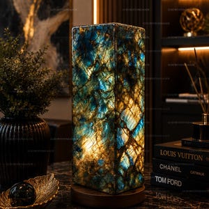 May include: A rectangular table lamp featuring a translucent stone shade with a vibrant blue and gold marbled pattern, illuminated from within, set upon a circular dark wooden base, creating a glowing effect with visible natural veining.