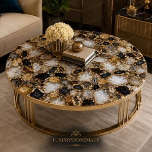May include: A round coffee table featuring a tabletop composed of polished, multi-colored agate slices in shades of black, white, and amber. The table is supported by a circular gold-toned metal frame with vertical bars and a smooth base.