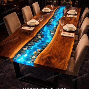 Peut inclure: Table de salle à manger en bois avec une rivière centrale en résine bleue et des pierres incrustées. La table est dressée avec des assiettes, des couverts et des verres à vin. Elle repose sur des pieds en métal noir.