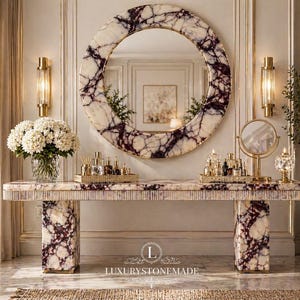Könnte beinhalten: Eine luxuriöse Marmorkonsole mit passendem rundem Spiegel. Tisch und Spiegel weisen ein weißes und violett geädertes Muster auf. Goldene Wandleuchten und ein Schminkspiegel flankieren den Spiegel. Eine Vase mit weißen Blumen steht auf dem Tisch.