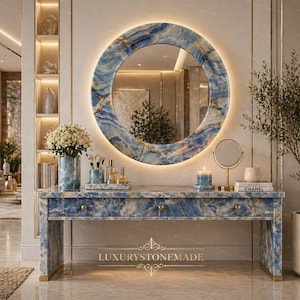 May include: A luxurious vanity table with a blue and gold marble design, featuring a matching round mirror with a backlit frame. The vanity has drawers and is adorned with a vase of flowers, makeup brushes, and perfume bottles.