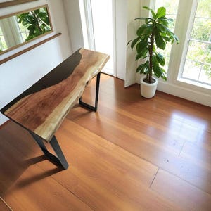 May include: A live edge wooden console table with a black epoxy resin inlay. The table has a natural wood grain finish and sits on black metal legs. The table is approximately 152 cm long.