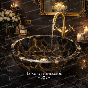 Puede incluir: Un lavabo de piedra redondo, negro y dorado, con un acabado pulido. El lavabo está colocado en una encimera oscura con un grifo dorado. El texto "LUXURYSTONEMADE" es visible en el lavabo.