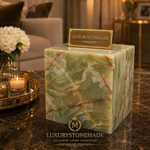 May include: A square, green onyx stone block with a gold-toned sign that reads "LUXURYSTONEMADE." The stone has a natural, marbled appearance with veins of white and brown. The base of the block has the text "LUXURYSTONEMADE EXCLUSIVE STONE FURNITURE."