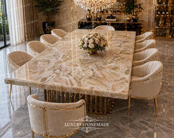 May include: A large dining table with a light-coloured, patterned stone top. The table is surrounded by ten beige upholstered chairs with gold trim. A floral arrangement sits in the centre. The table base is gold.