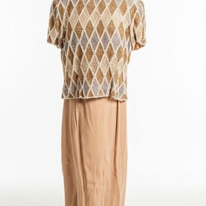 Puede incluir: Un conjunto vintage de dos piezas. La parte superior es una blusa de manga corta con cuello alto, con un patr&oacute;n de diamantes en dorado, beige y gris. La parte inferior es una falda larga y fluida en color beige liso. El conjunto se exhibe en un maniqu&iacute;.