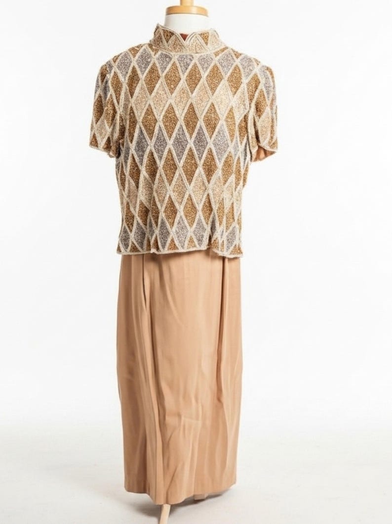 Puede incluir: Un conjunto vintage de dos piezas. La parte superior es una blusa de manga corta con cuello alto, con un patr&oacute;n de diamantes en dorado, beige y gris. La parte inferior es una falda larga y fluida en color beige liso. El conjunto se exhibe en un maniqu&iacute;.