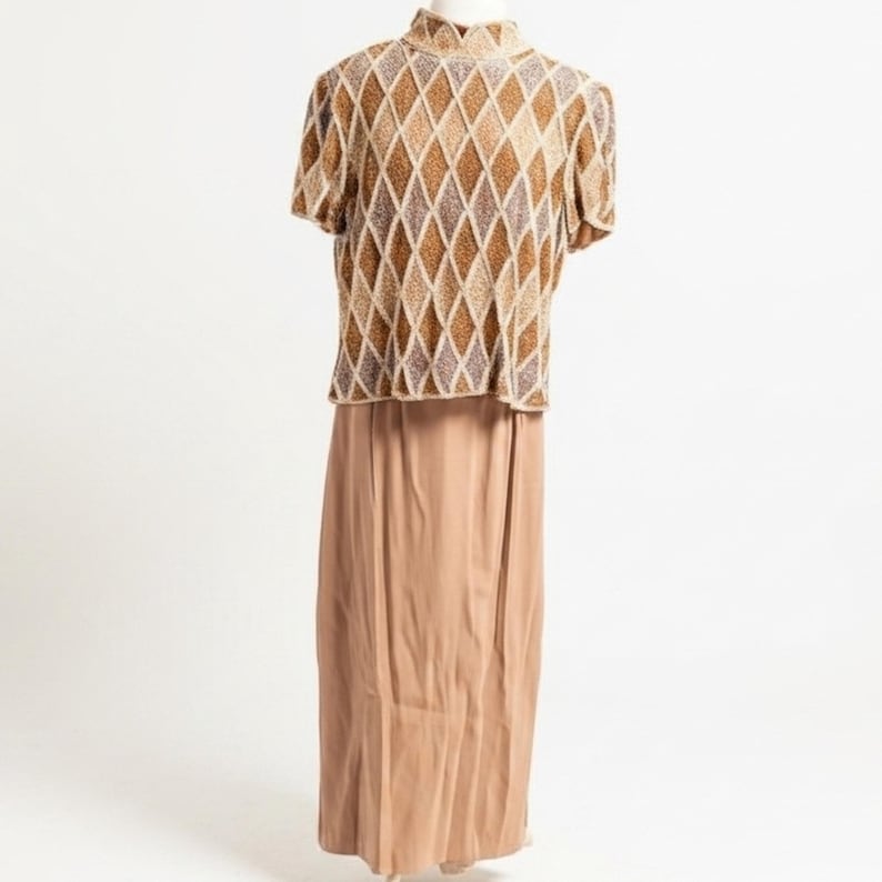 Puede incluir: Un conjunto vintage de dos piezas con una blusa de manga corta y una falda larga. La blusa tiene un cuello alto y un estampado de rombos en tonos marr&oacute;n, beige y dorado. La falda es de color marr&oacute;n claro liso y fluida.