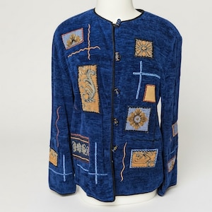 May include: A long-sleeved blue jacket featuring a textured fabric with various rectangular patches in shades of gold, tan, and light blue. The garment includes a round neckline, a front button closure with dark toggles, and decorative embroidery.